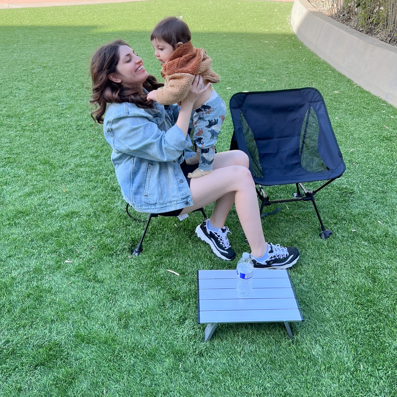ATEPA Ultralight Tall Camping Chair used by a mother on a green lawn, providing stable support for holding a baby during outdoor family time