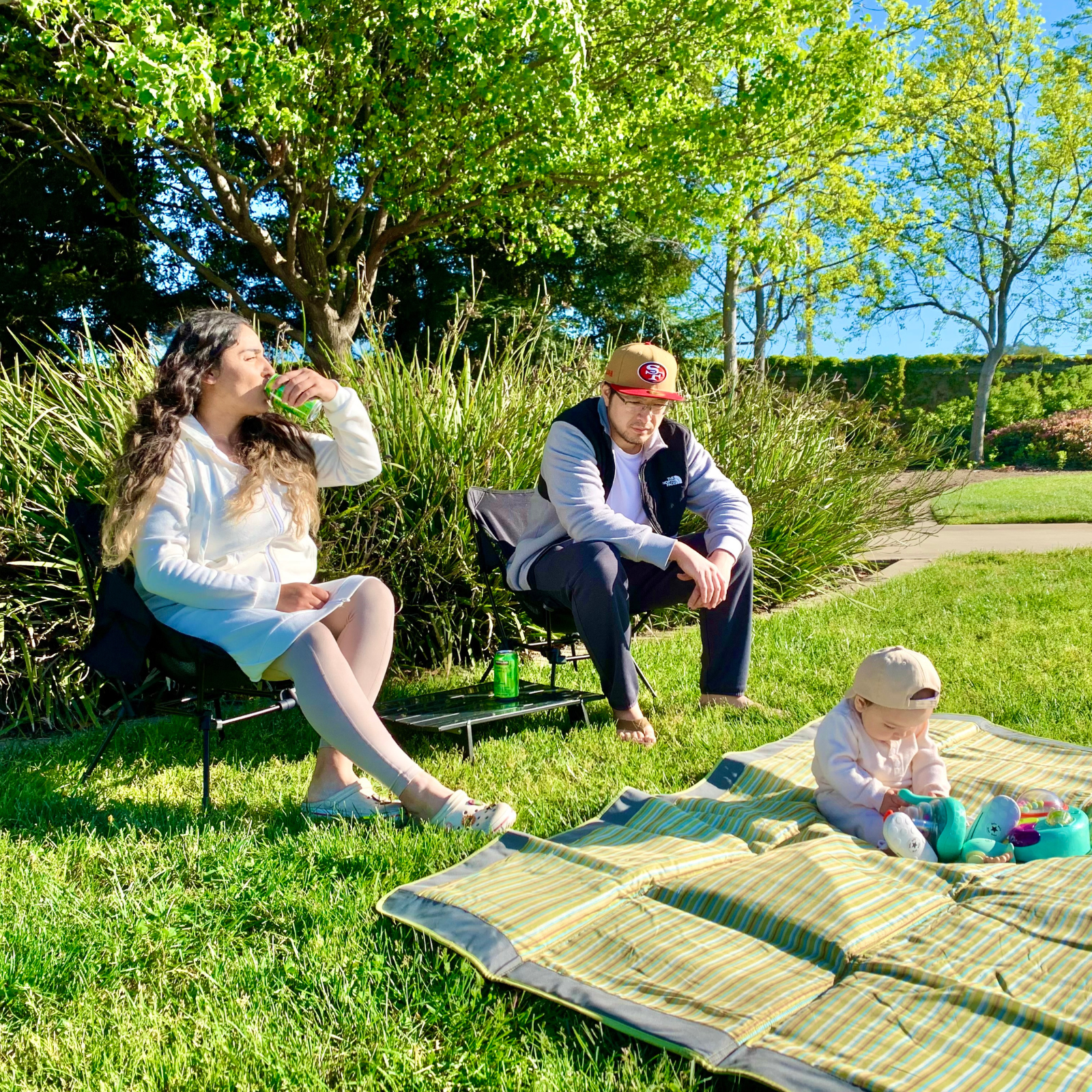 ATEPA Tall Camping Chairs providing comfortable seating for a couple during a sunny family picnic on a green lawn with a baby playing